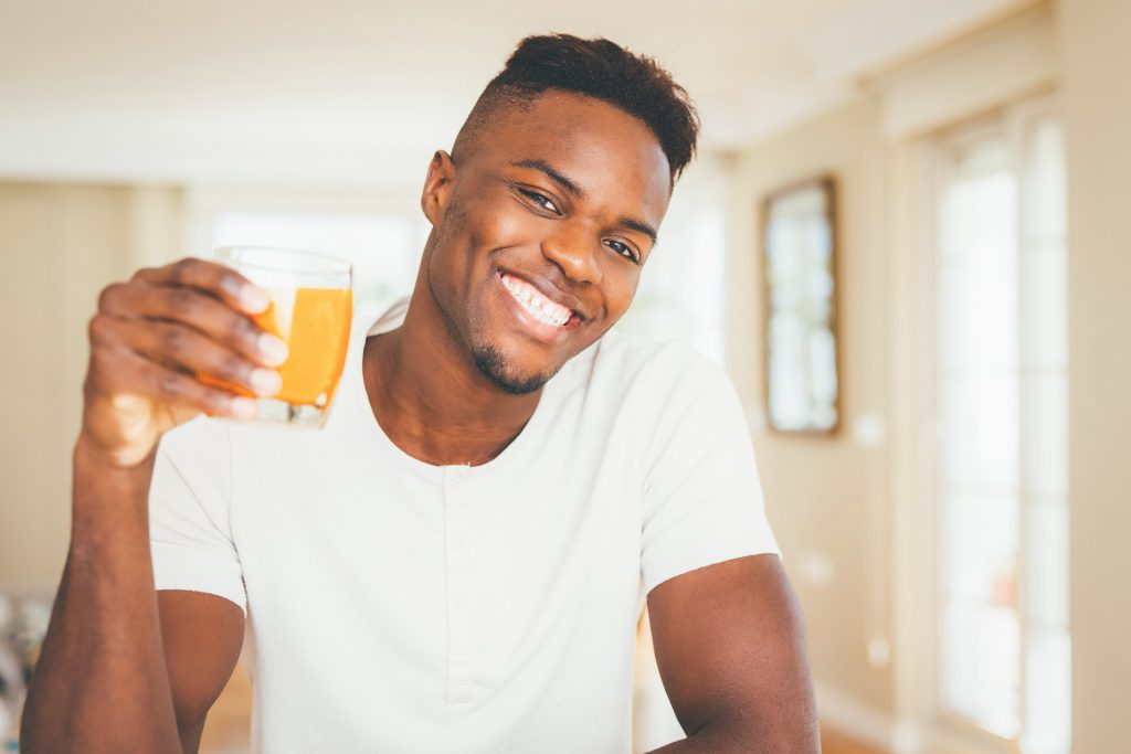 Handsome young african man drinking a glass of fresh natural ora